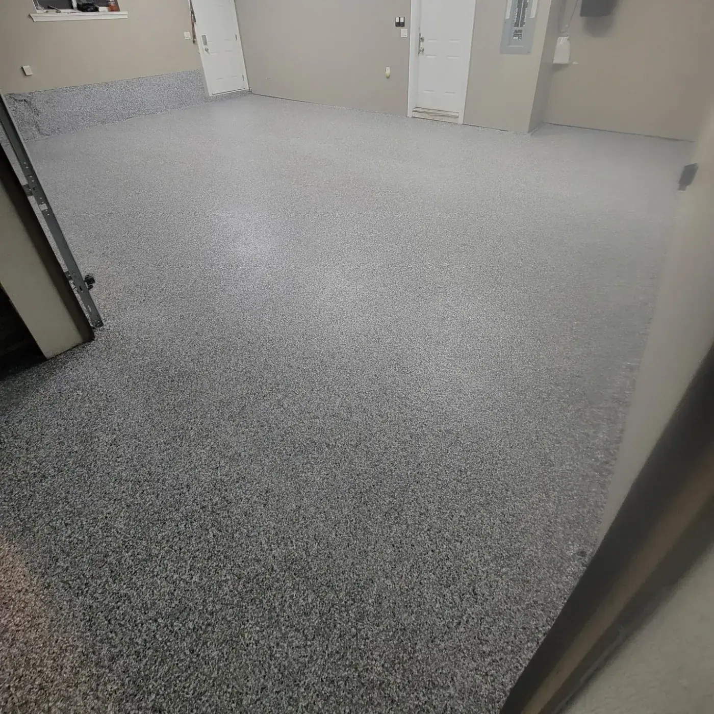 Interior garage bay with a grey and white flake floor running back to two white doors and an electrical panel.