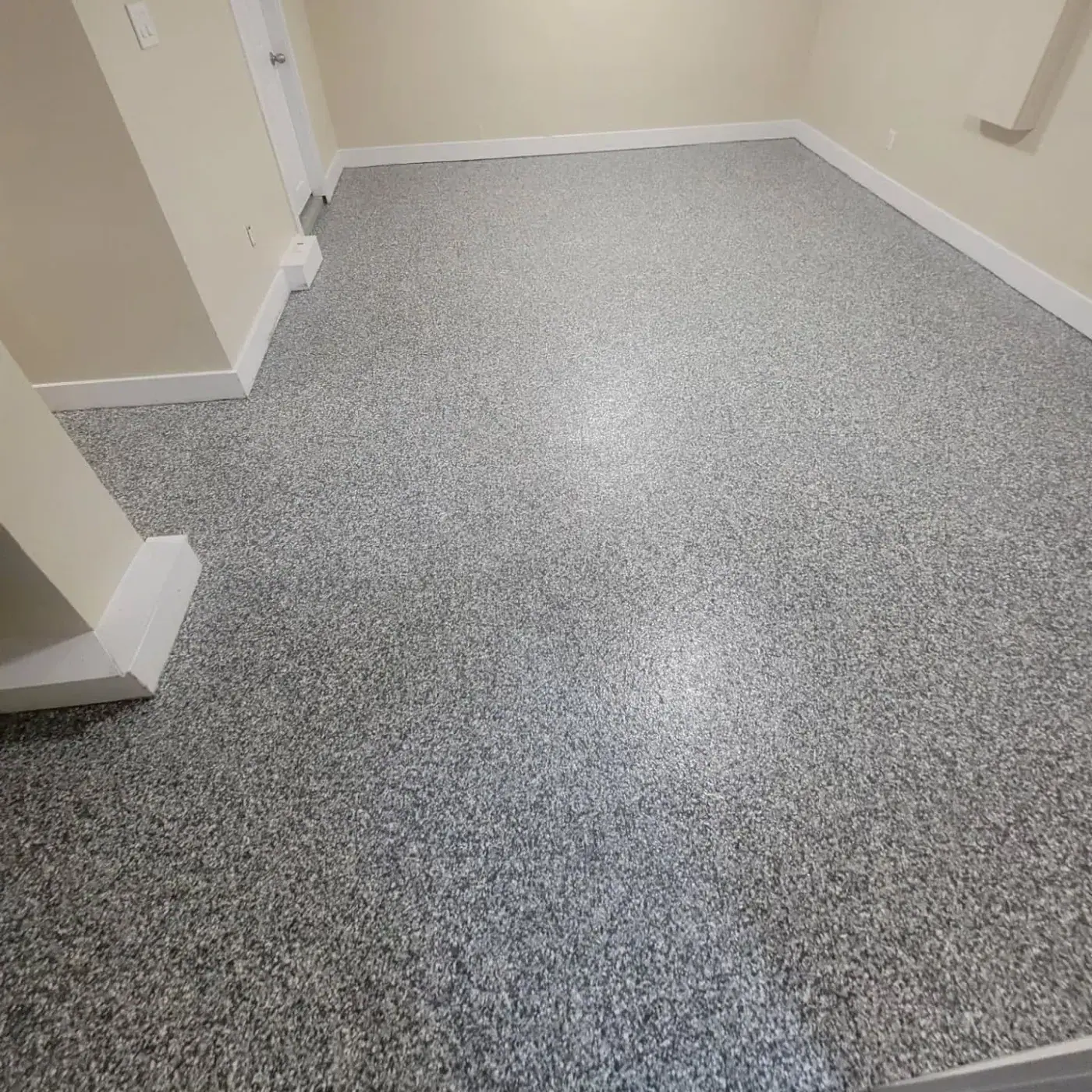 Interior room with a grey and white flake floor, white baseboards and an open doorway to a hall.