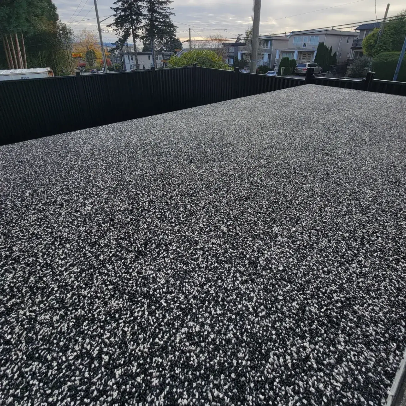 Roof deck finished in black and white rubber granules at dusk, enclosed by a tall black fence.