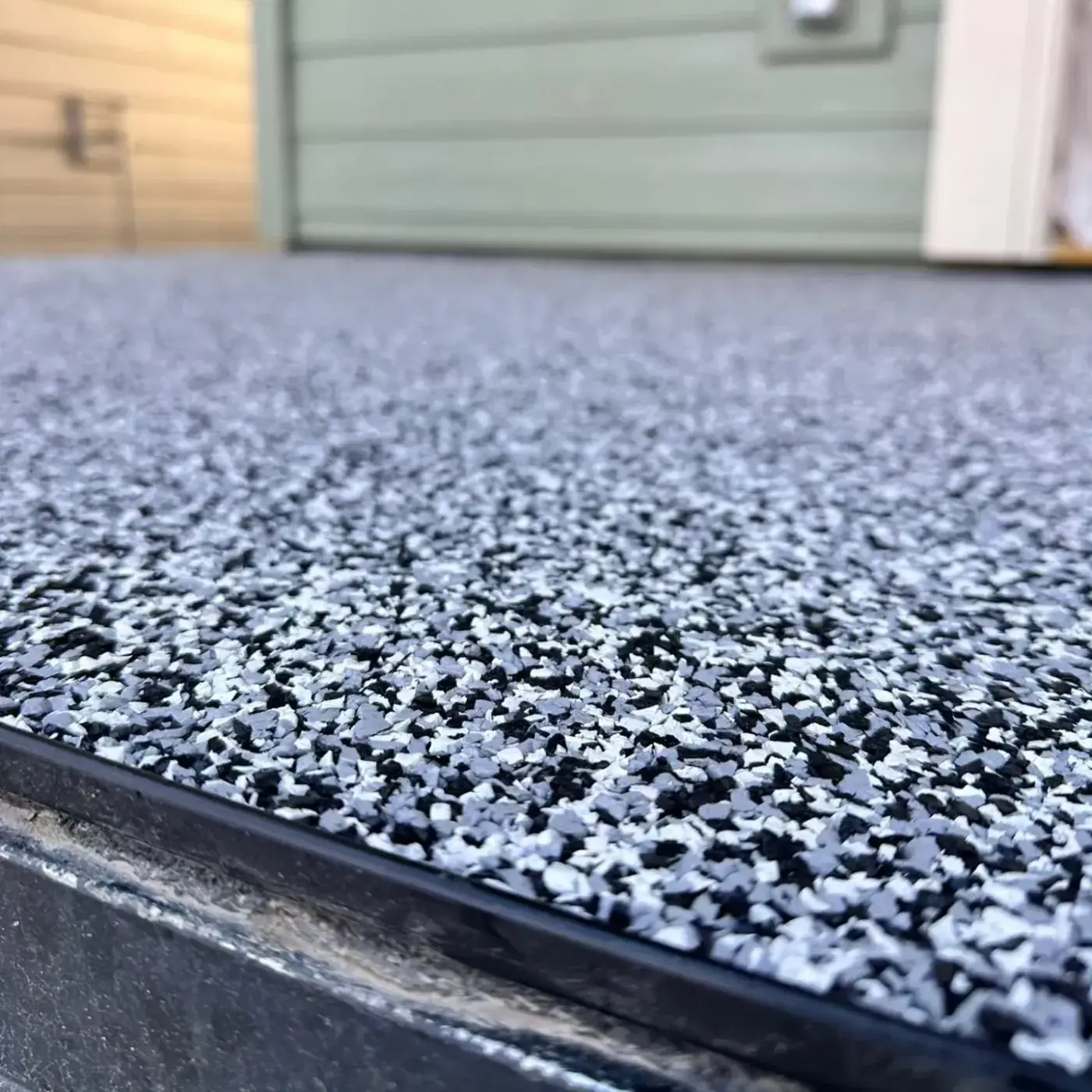 Close view of the edge of a grey, black and white rubber granule surface meeting a metal trim strip.