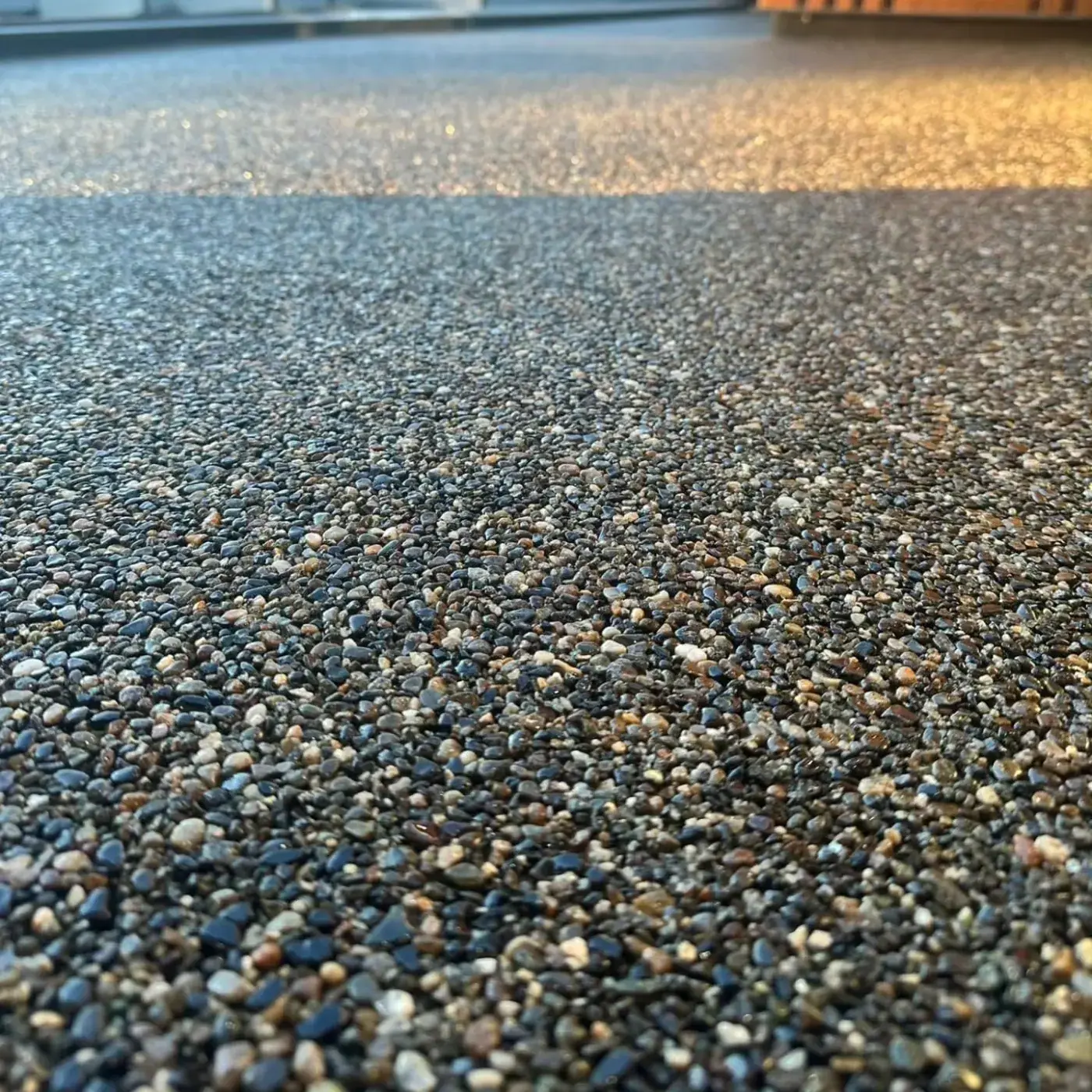 Close view of stone surfacing in low evening sun, showing rounded pebbles bonded into a level surface.