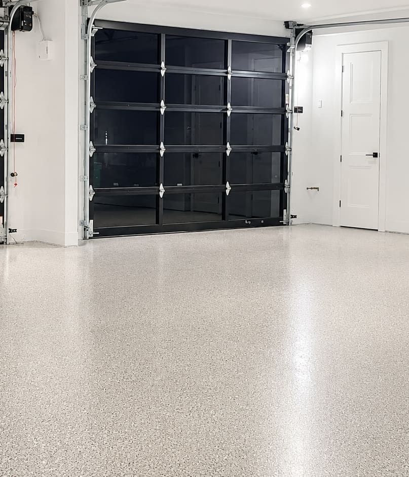 A double garage with a grey and white flake epoxy floor, black framed glass garage doors and white walls
